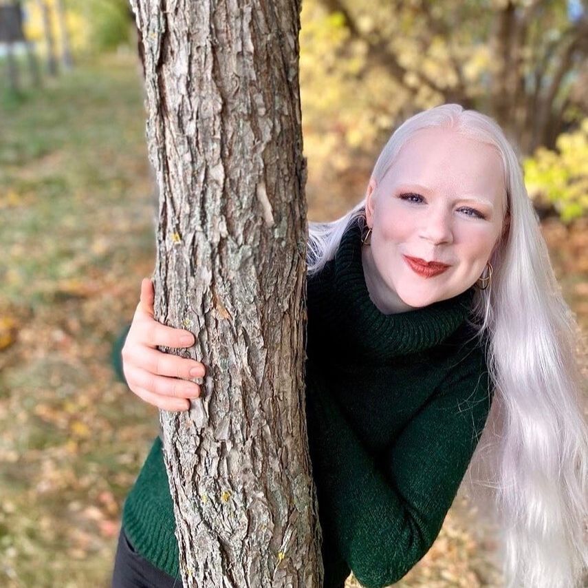 Tamara peeking out from behind a tree smiling coyly