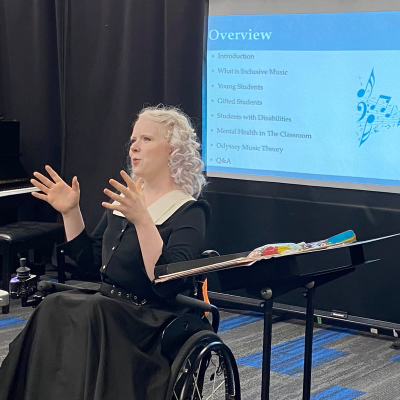 Tamara presenting In front of A Slide Show presenting to a room of people. She is sitting in her wheelchair. Picture