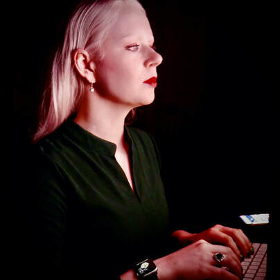 Tamara sits at a computer in a darkly lit room working on a presentation