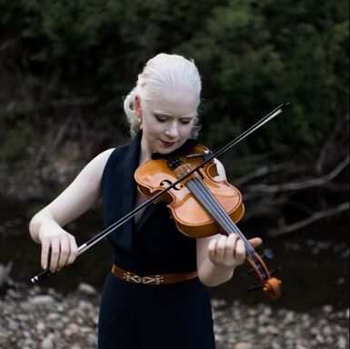 Tamara with a serene look on her face playing the violin in the woods