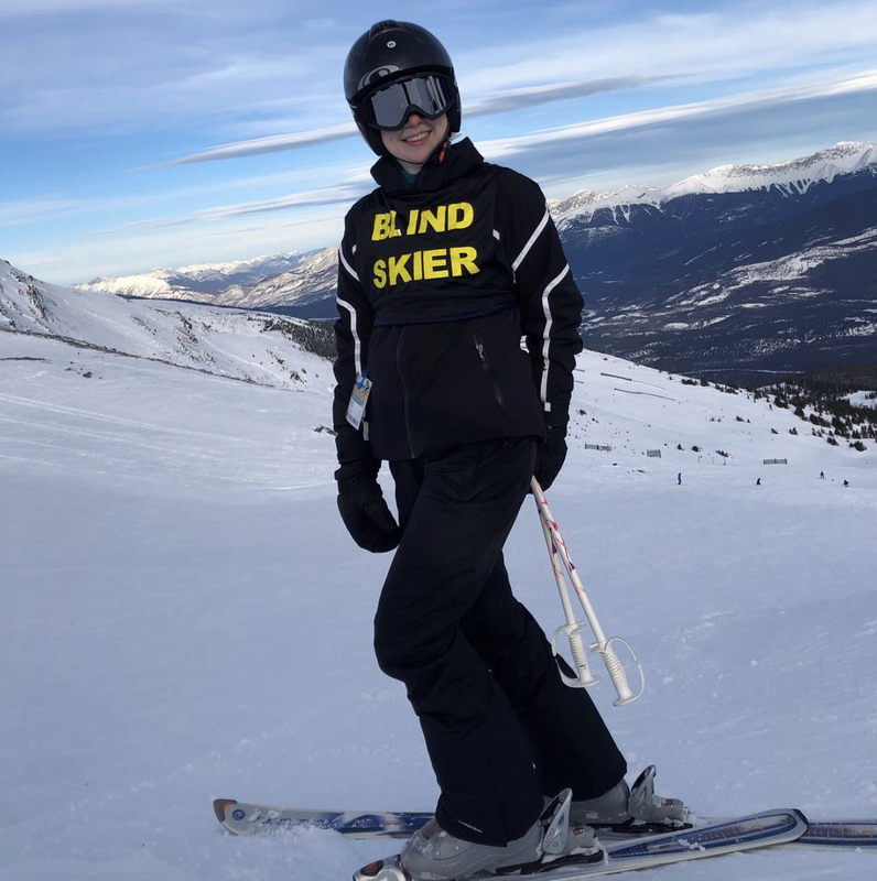 Tamara wearing a blind skiier pinnie at the top of a mountain